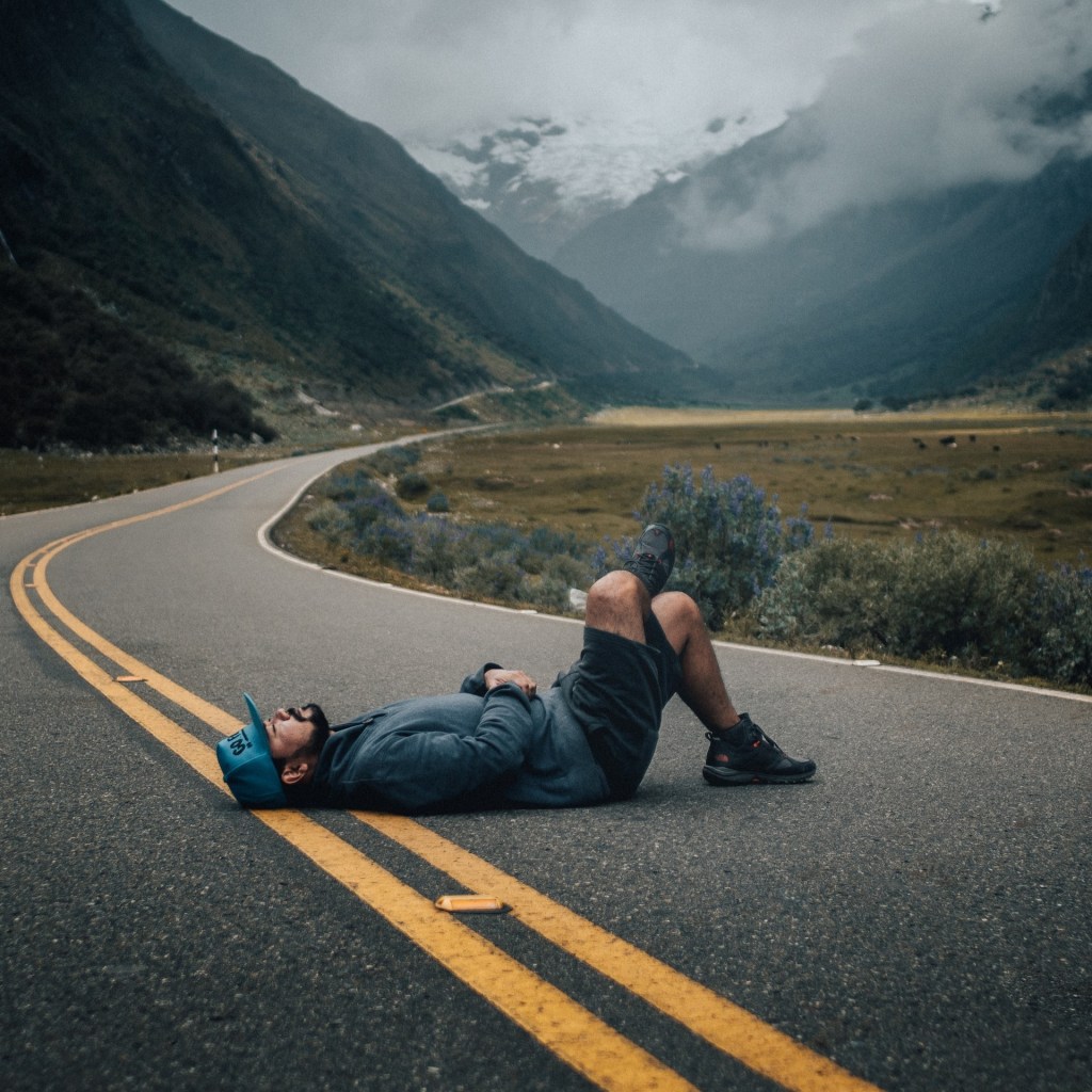 A man lying down and resting in a winding country road. 